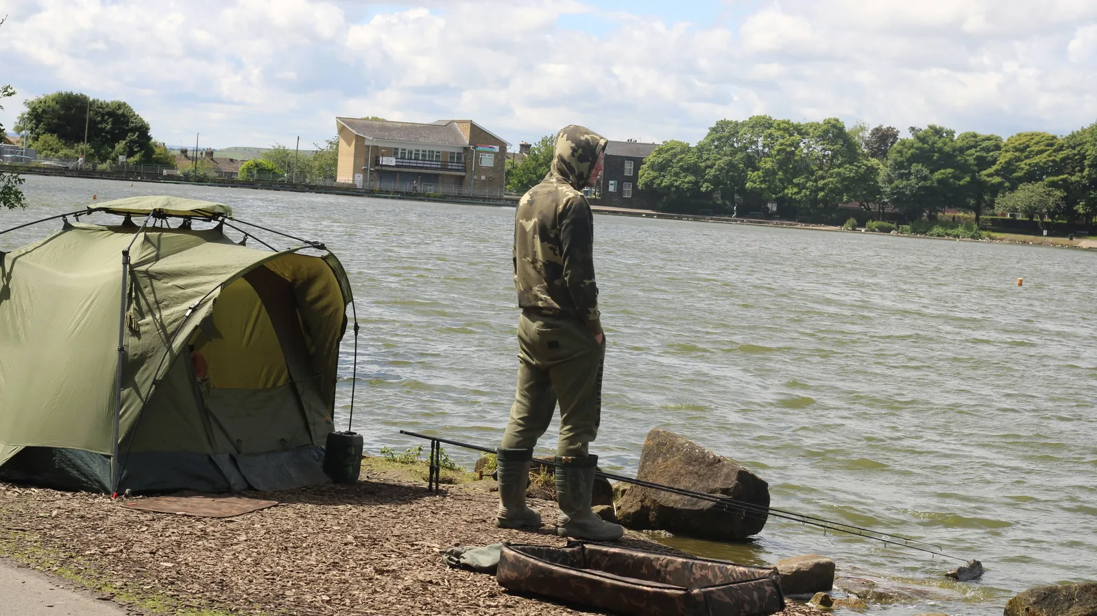 Puesto completo de carpfishing junto al agua con rod pod, alarmas, bivvy y silla al atardecer