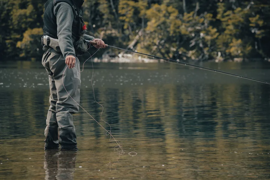 Pescador con vadeadores de neopreno adentrándose en aguas de un río de montaña