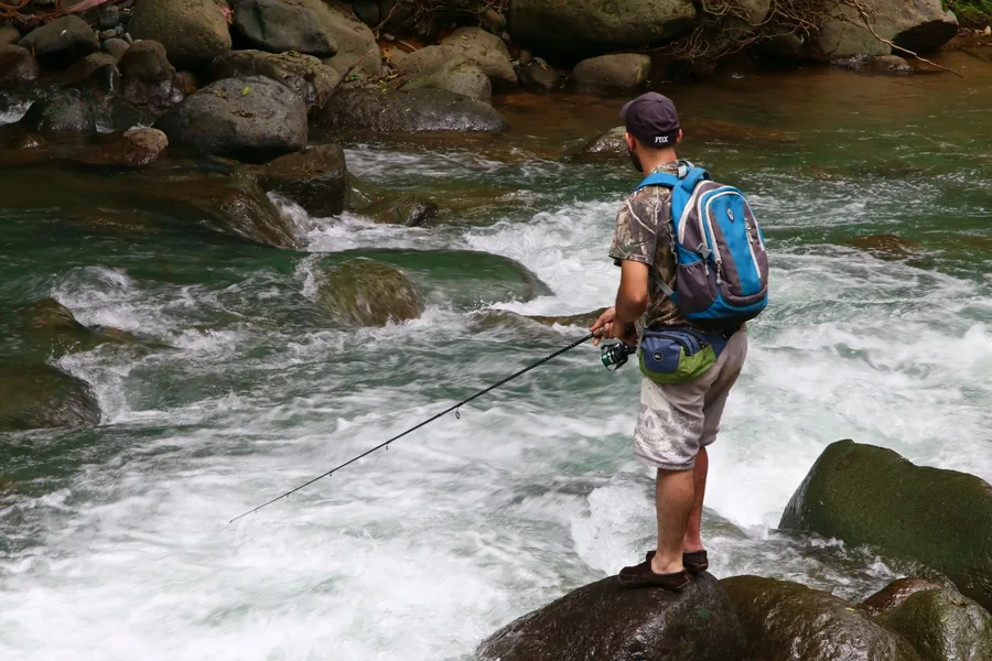 Mochila técnica de pesca con cajas de señuelos organizadas, junto a un río