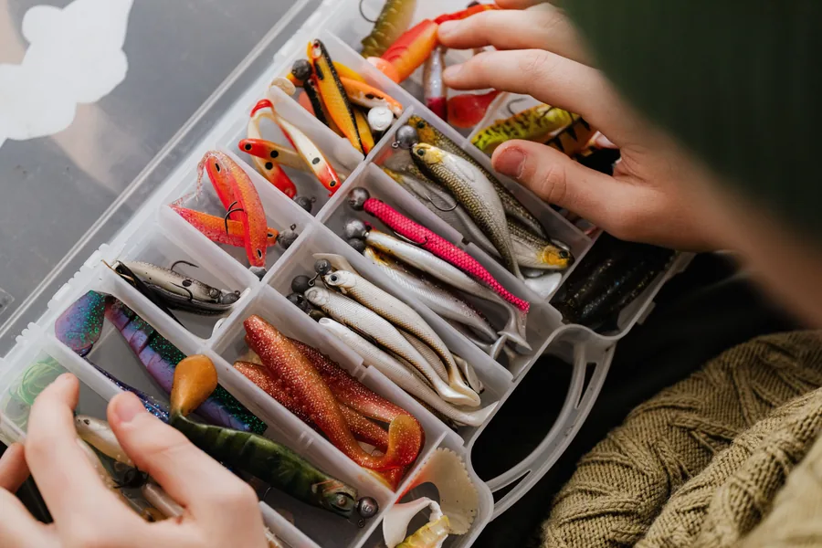 Caja de pesca abierta con compartimentos organizados llenos de señuelos y vinilos