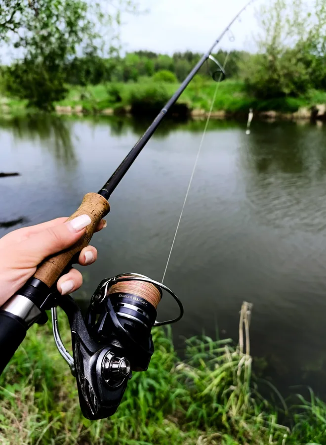 Pescador lanzando con una caña de spinning y carrete de bobina fija montado, en un lago