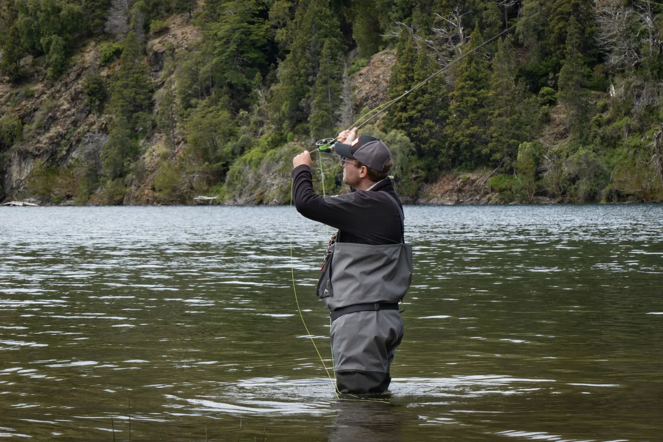 Pescador con vadeador y chaleco multibolsillos entrando en el río para pescar a mosca