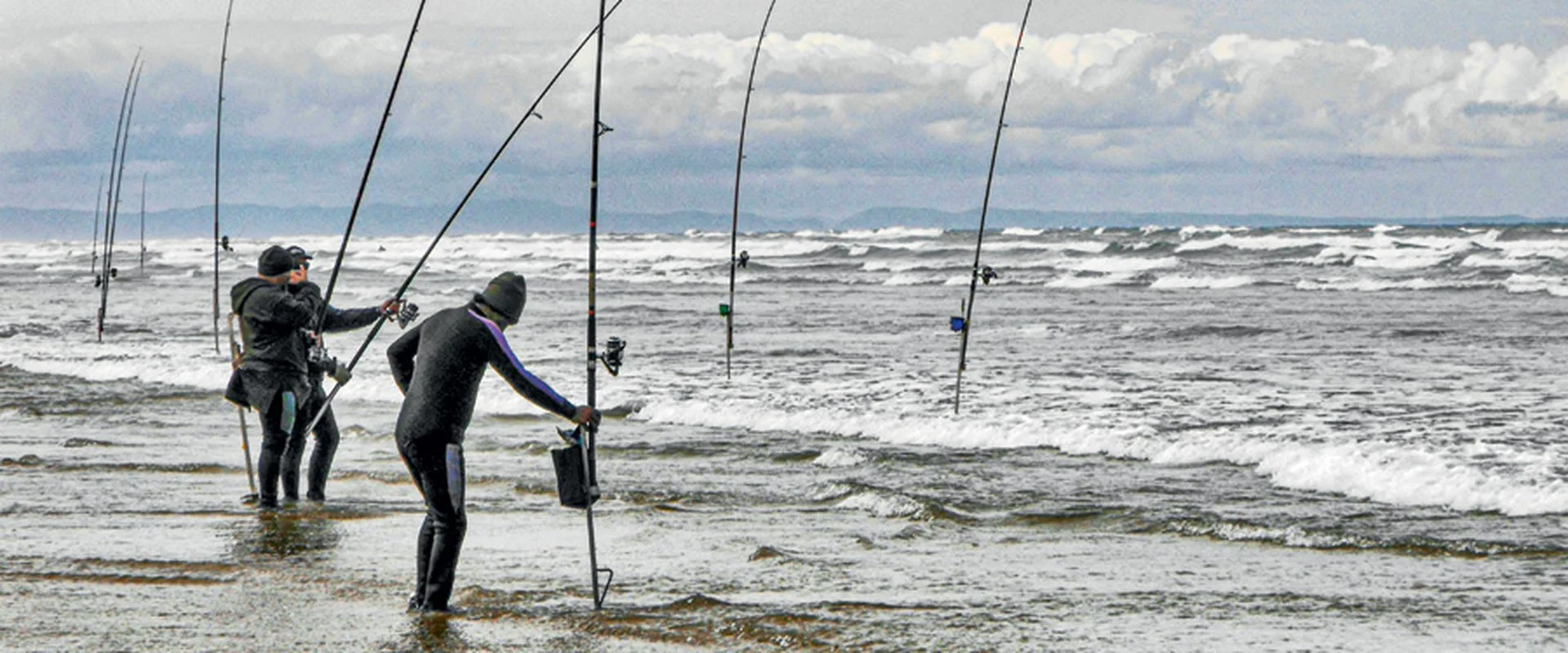 Pescador practicando spinning y surfcasting desde una playa española, mar de fondo